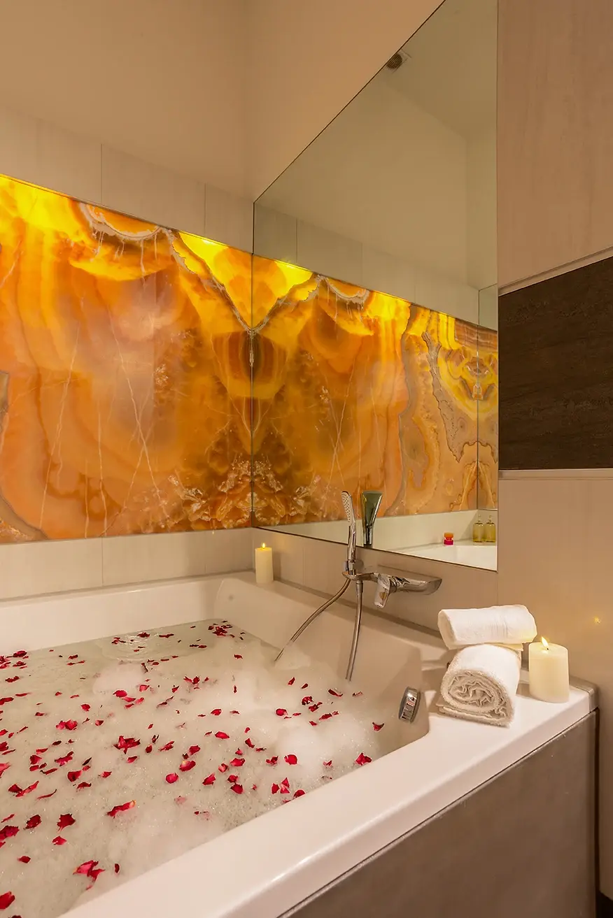 Bath with rose petals and candles in front of a backlit onyx wall